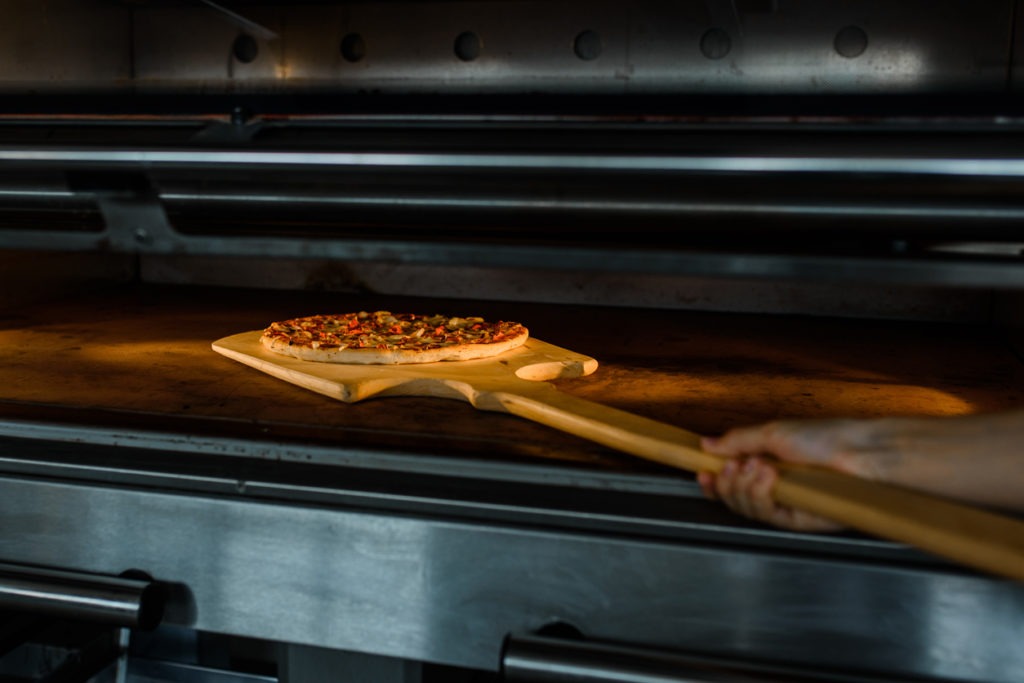 A wooden pizza peel inside an oven with a pizza on top