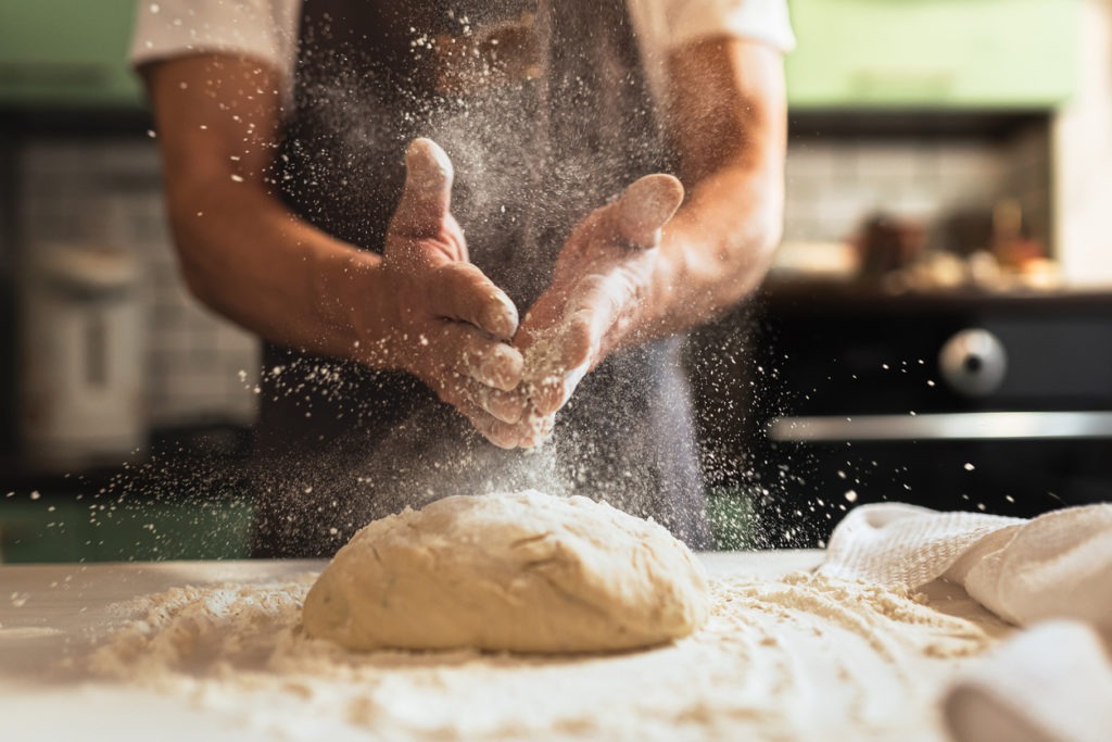 Chef’s hand spraying flour over the dough
