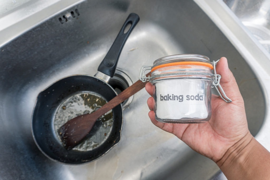 Cropped picture of a hand holding a container of baking soda at the washbasin