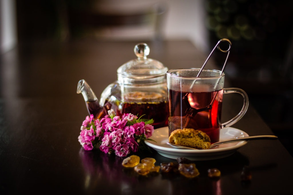 Glass of tea with tea ball and teapot on wooden table