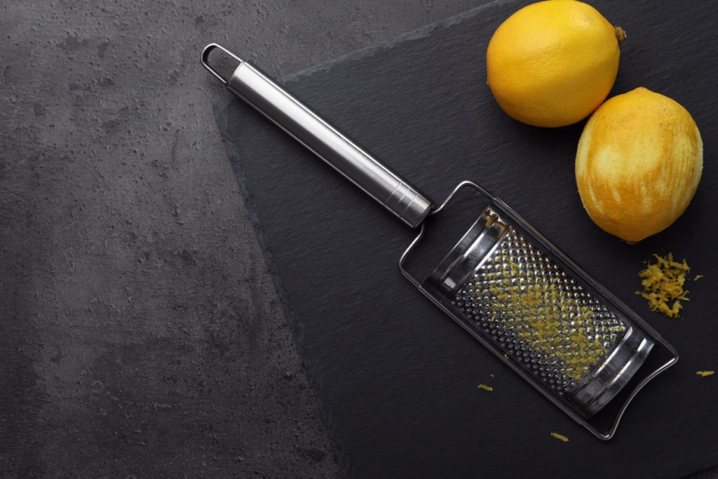 Grater and fresh lemons on black table, flat lay. Space for text