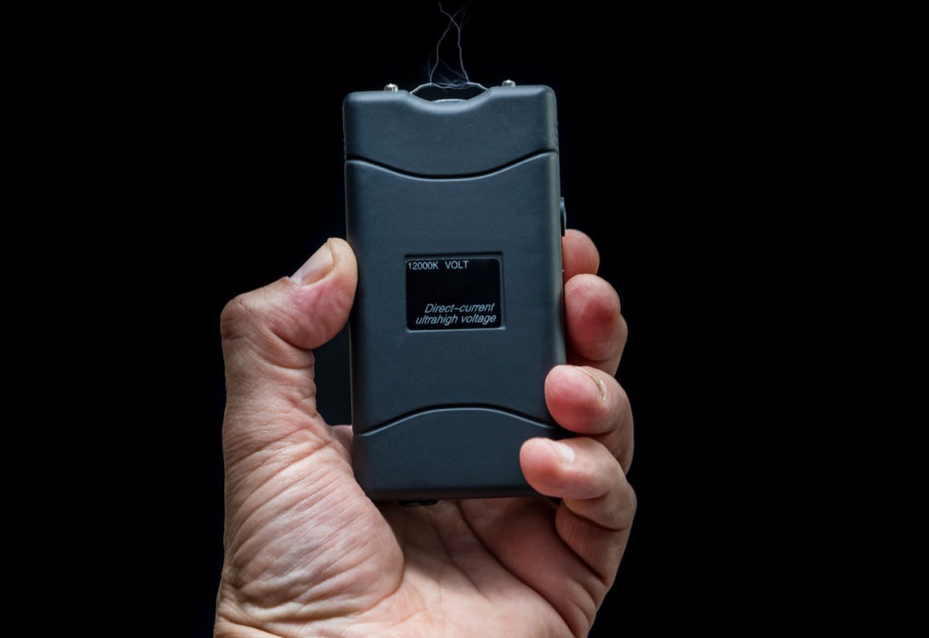 Hand holds a Taser in front of black background