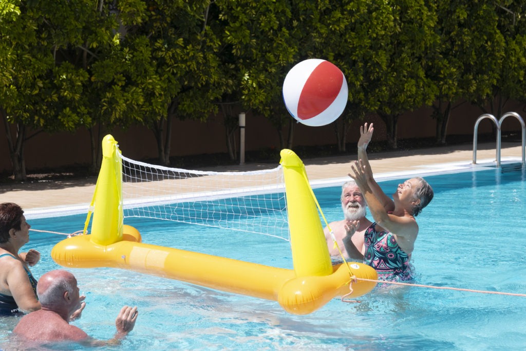 Have fun in the swimming pool with an inflatable net and ball. Four people, two elderly women, and men. The bright light of the sun