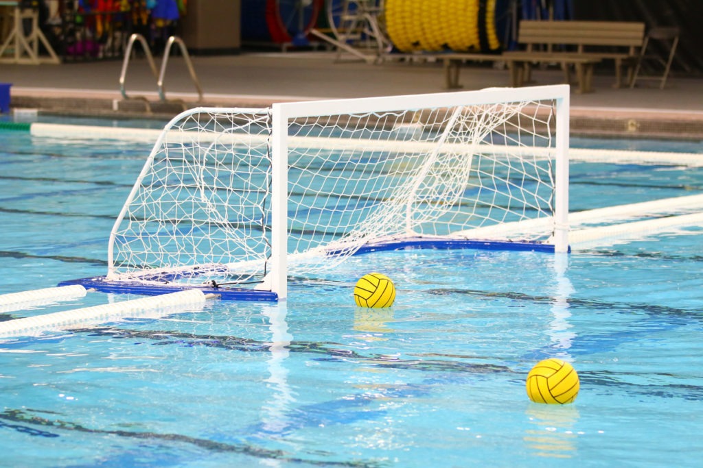 Indoor photo of two yellow water polo balls floating on the water near the goal net