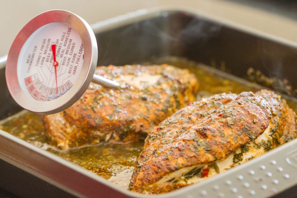The temperature is measured of two seasoned chicken breasts in a baking tray