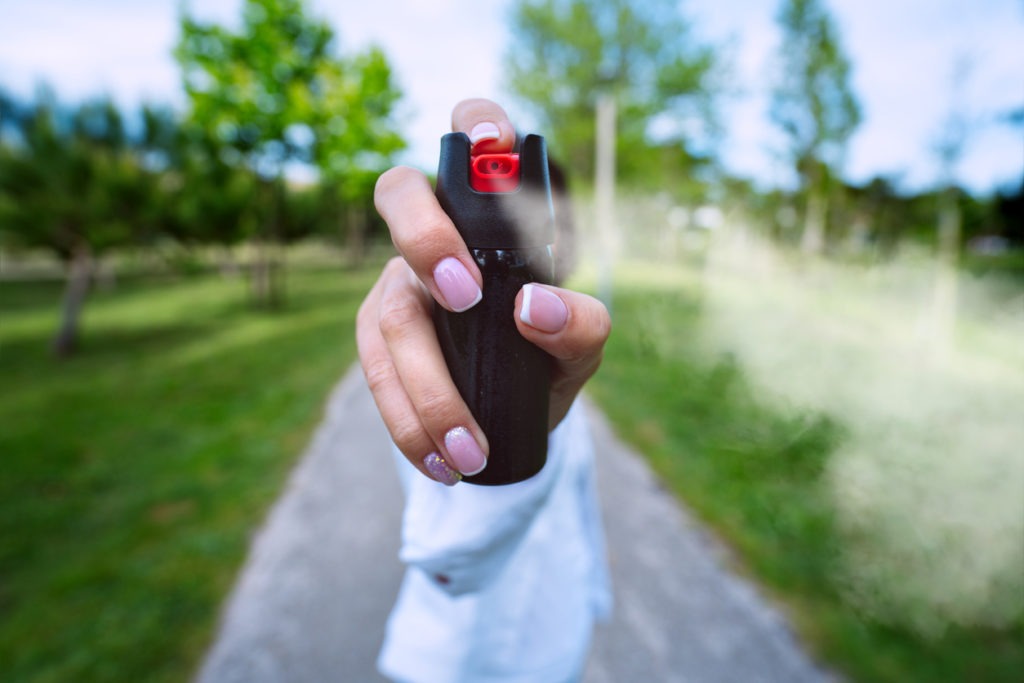 Woman using pepper spray or tear gas for self-defense outdoors.