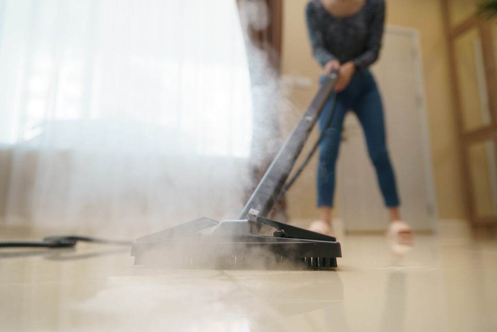 Woman washes the floor with a steam mop