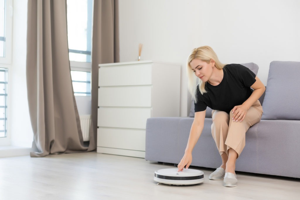 Young woman using automatic hybrid robot mop to clean the floor