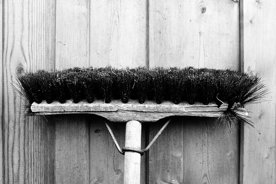 a black and white photo of a broom leaning upside down against a wooden wall