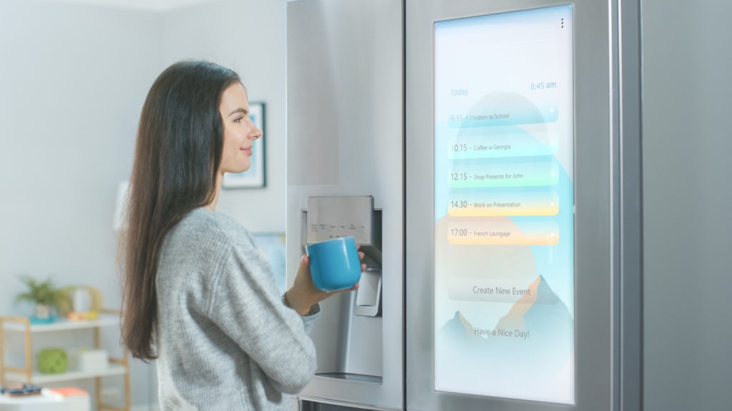 a woman reading something on the screen of a smart fridge