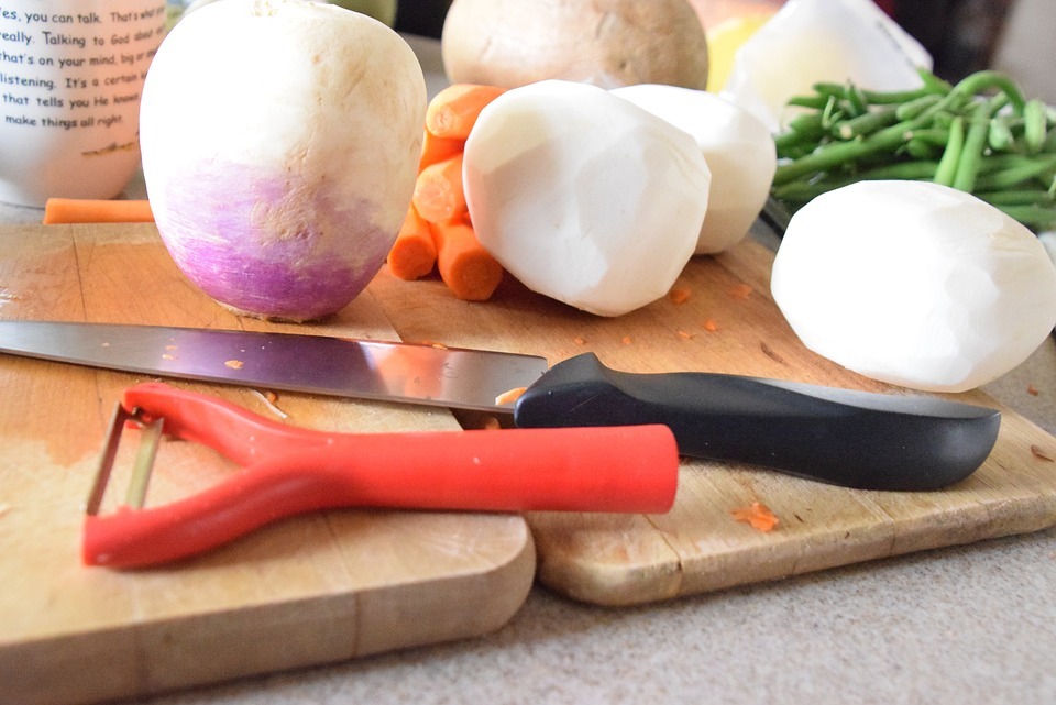 a y-peeler beside a knife and vegetables on top of a chopping board