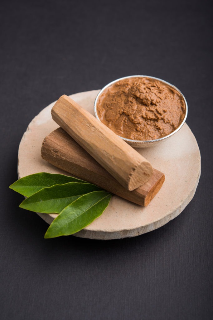Ayurvedic Chandan powder or sandalwood paste in silver bowl with sticks and leaves placed over sahan or sahana or circular stone base for creating paste