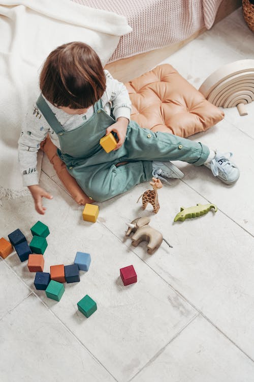 child in a white long sleeve playing with Lego blocks