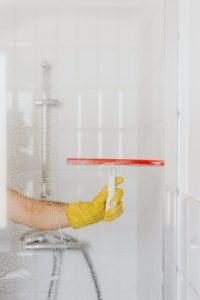 person-cleaning-a-glass-shower-using-a-squeegee-683x1024