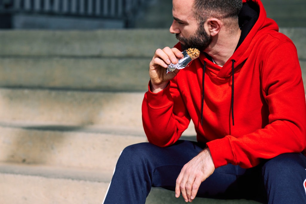 Tired sportsman sitting on stairs outdoors and eating energy bar