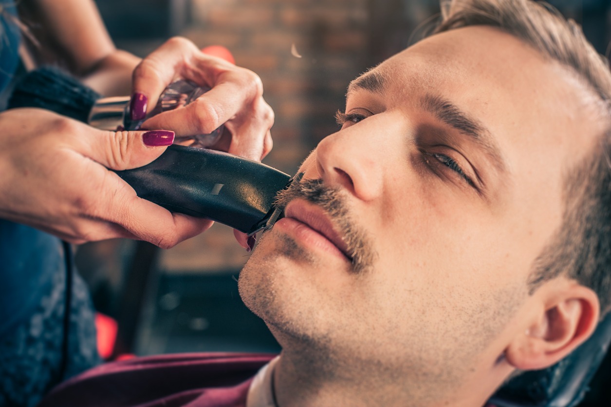 A barber trimming the mustache of a man