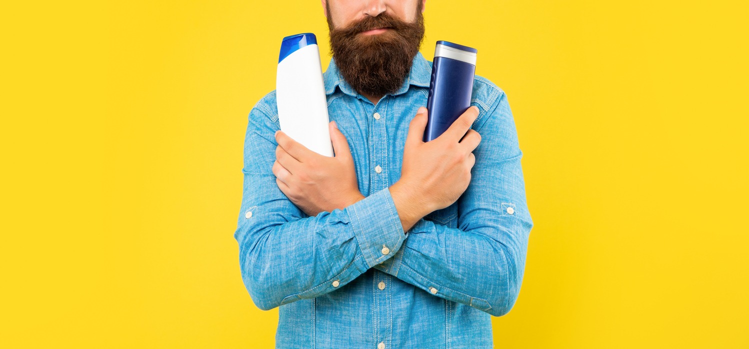 A bearded man holding a shampoo and conditioner