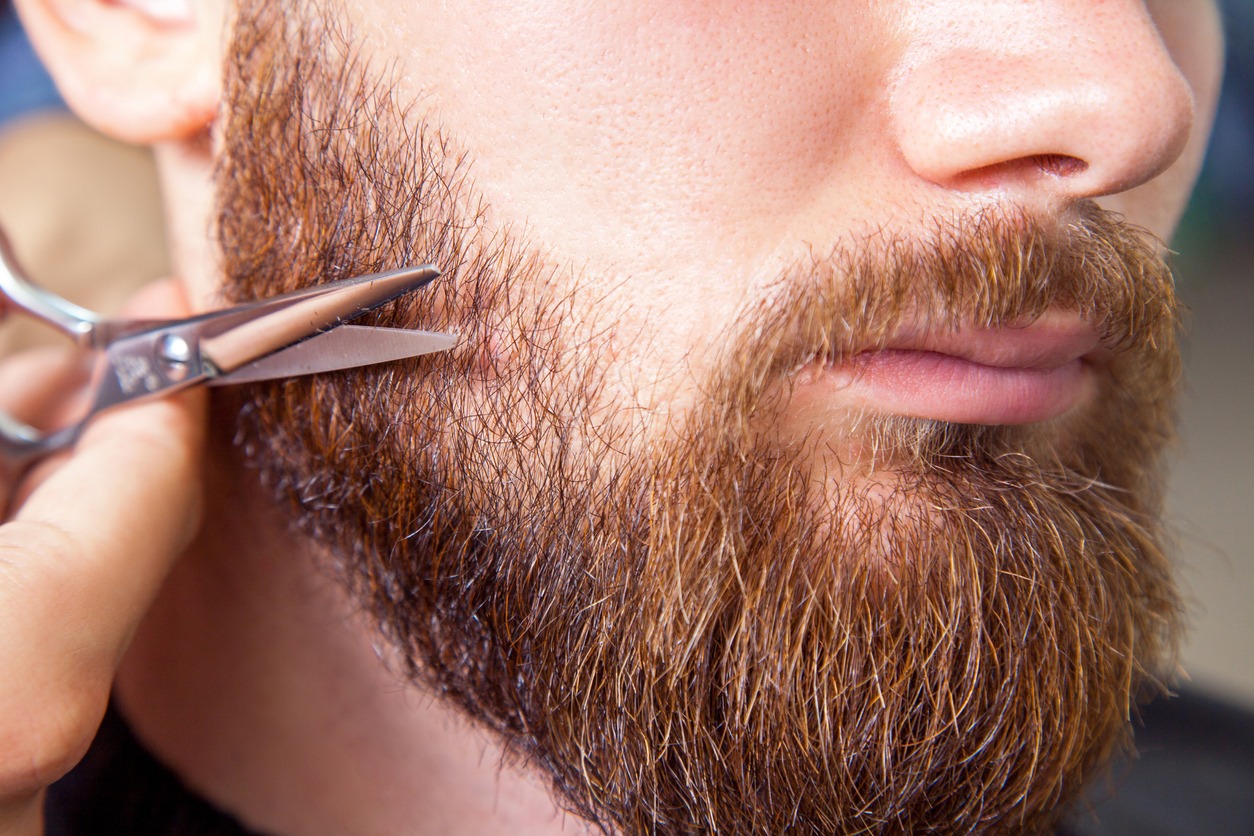 A man trims his beard using scissors