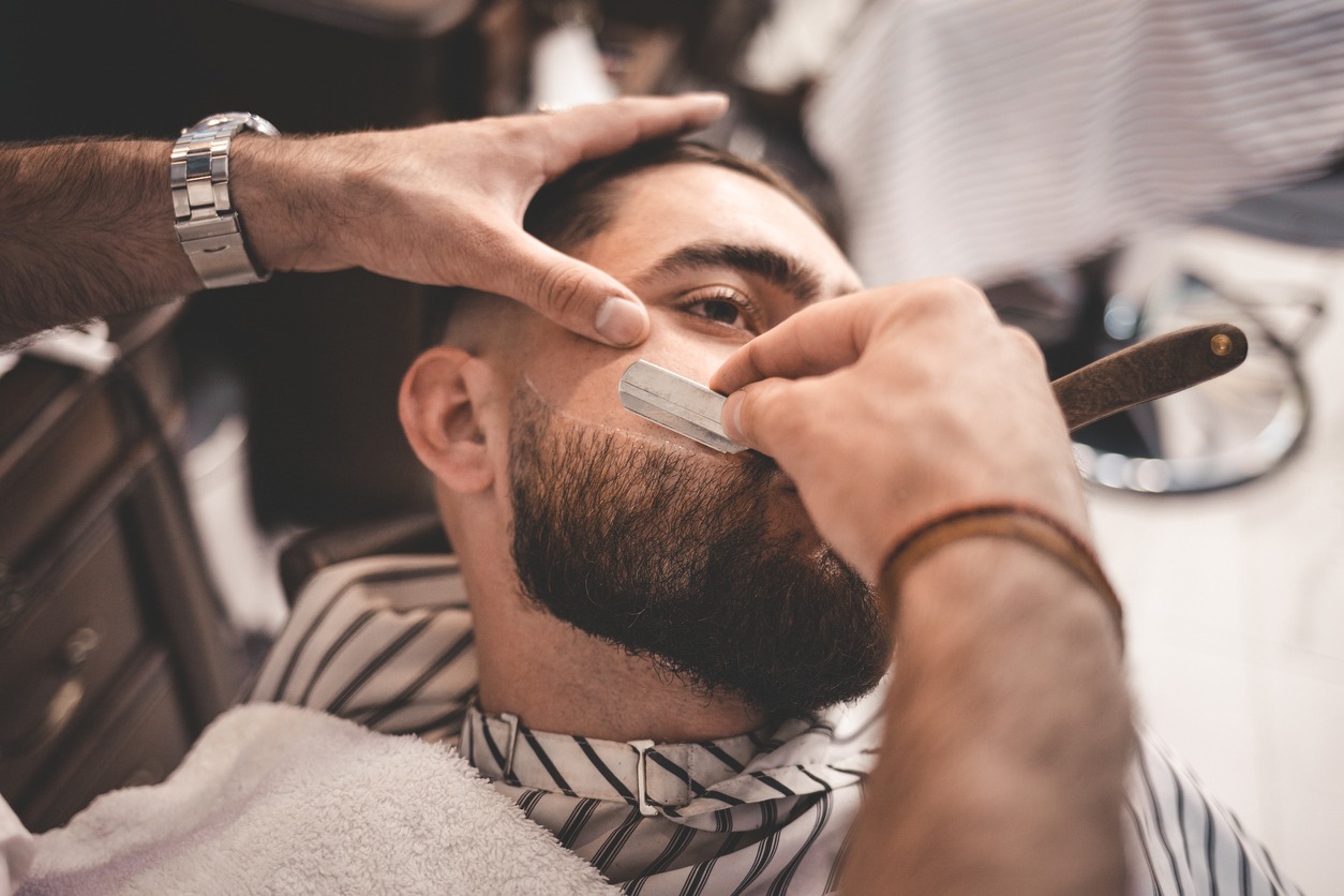 A man’s beard is being lined up using a razor