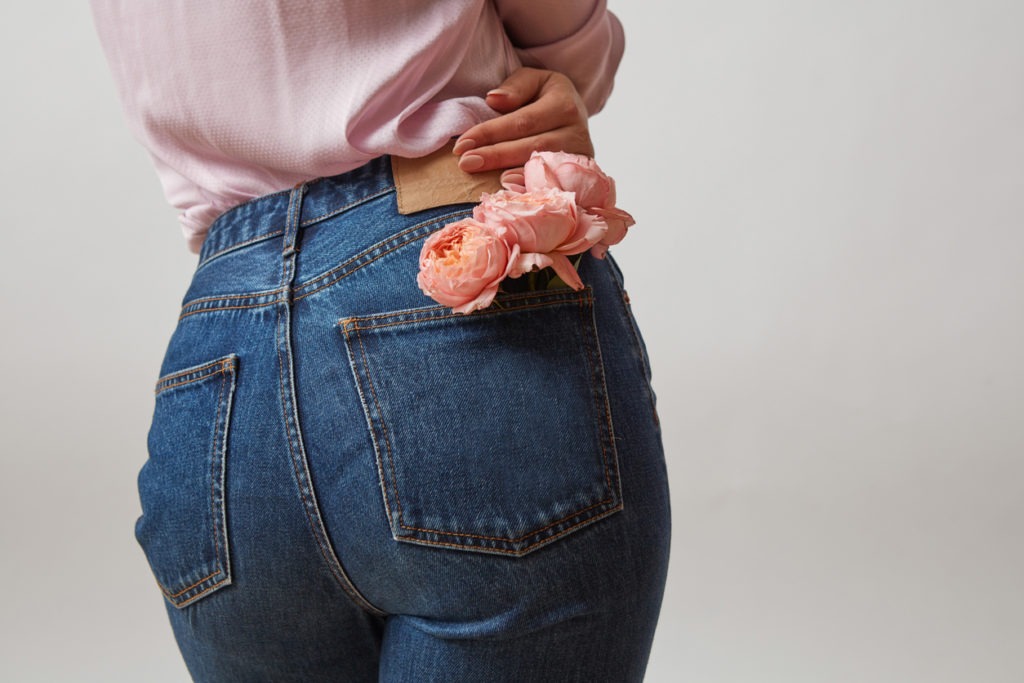Attractive woman's butt in a blue mom jeans and fresh roses living coral color in a back pocket