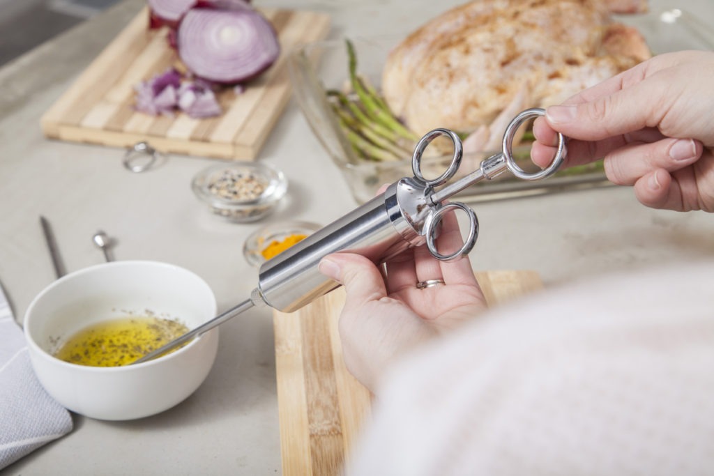 Cropped photo of a hand handling a stainless steel meat injector 