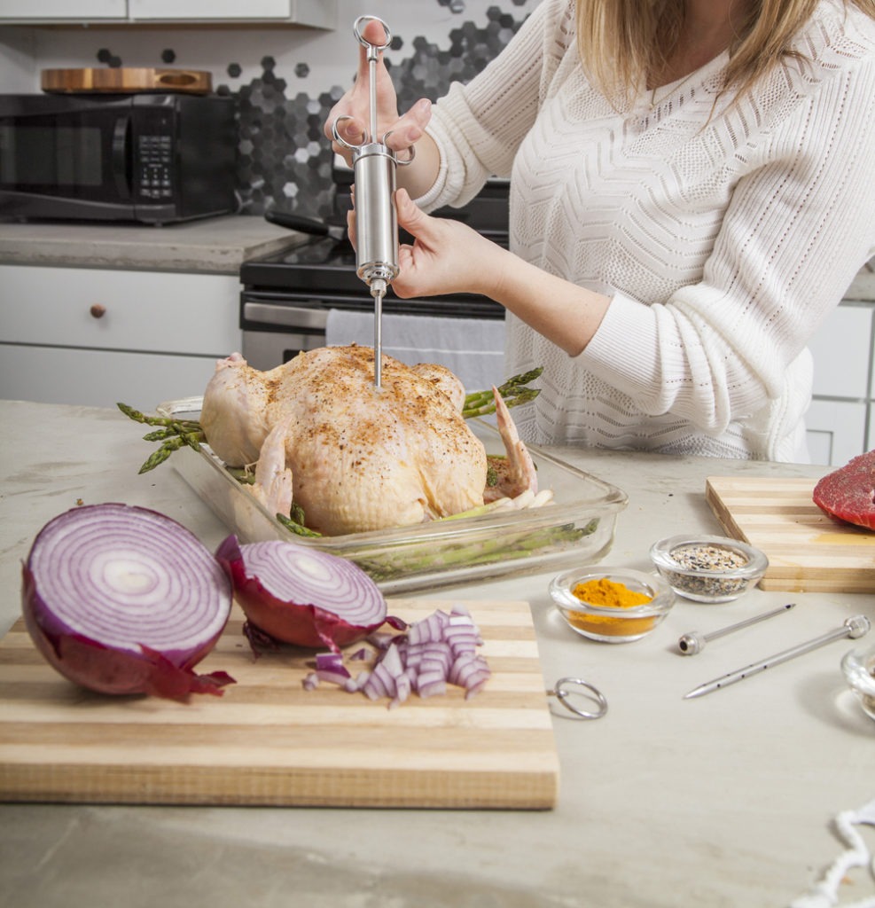 Cropped picture of a woman injecting butter into uncooked turkey.