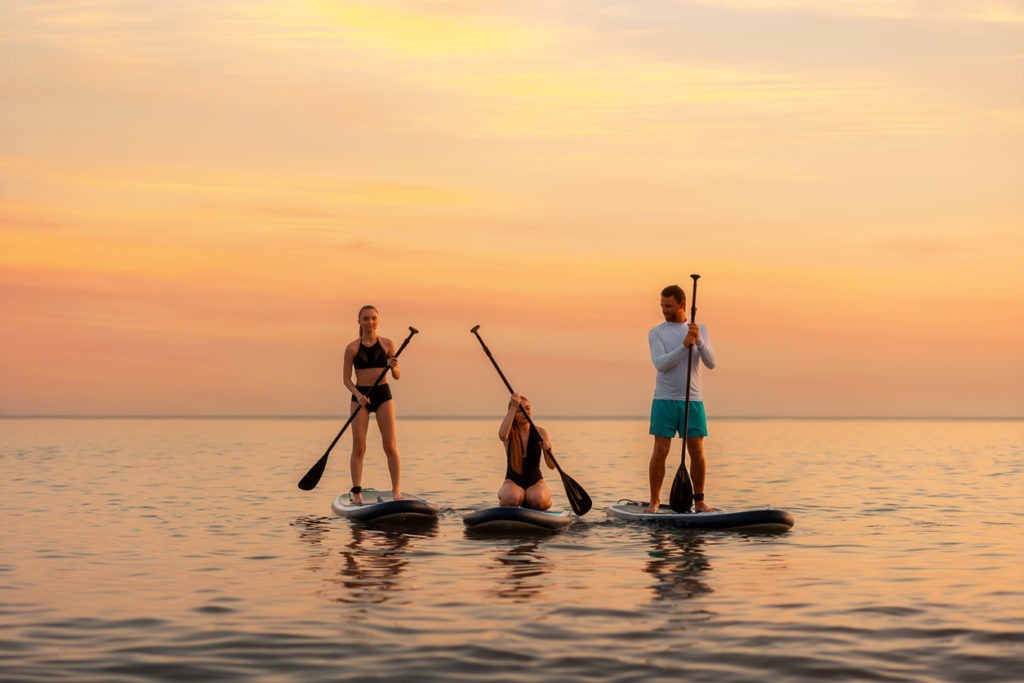 Group of Caucasian people swimming on a sup board at the ocean. Sport activity of friends on vacation. Summer sport and recreation