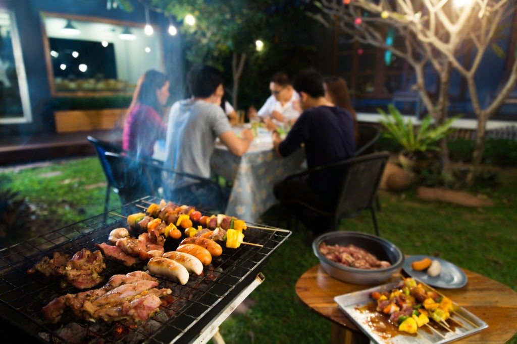 Image of a barbecue on top of a grill with a family eating dinner in the background