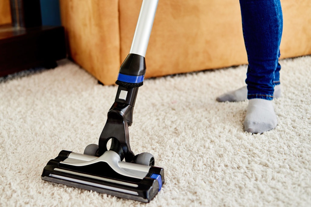 Person in jeans and socks vacuuming a carpet.