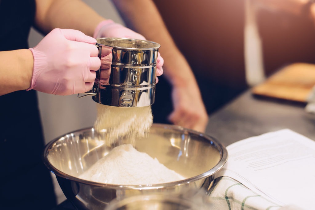  Woman sifting white flour to metal bowl in the kitchen