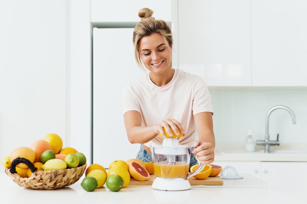 Young cheerful woman with a lot of citrus fruits during fresh orange juice preparation at home
