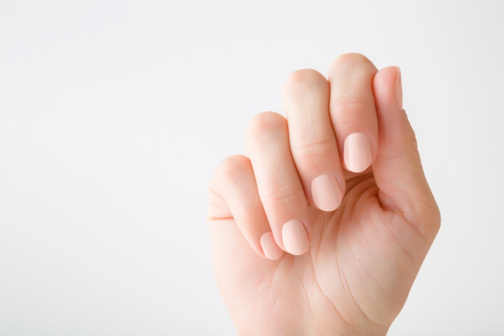 Young woman’s hands with beige-colored nails on light gray background