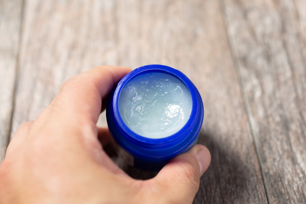 a hand while holding a blue vapor rub jar on a wooden table