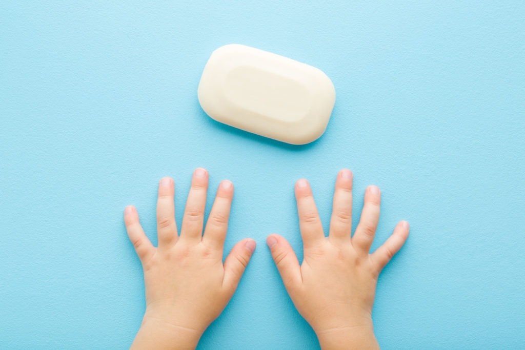 baby boy’s hand and white soap in pastel blue background