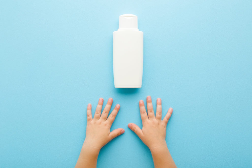 baby boy’s hands and a bottle of body wash in pastel blue background
