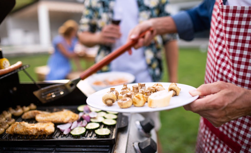 Midsection of family outdoors on garden barbecue, grilling
