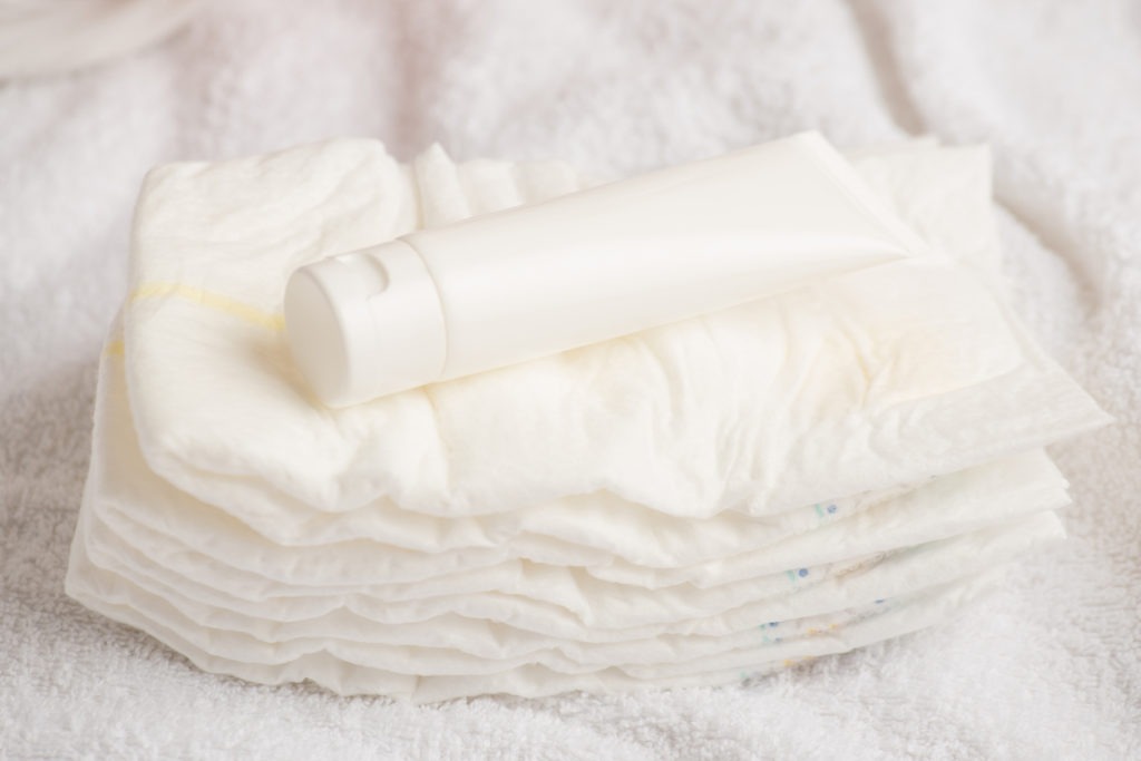nappy cream tube on top of stacked diapers in white textile background