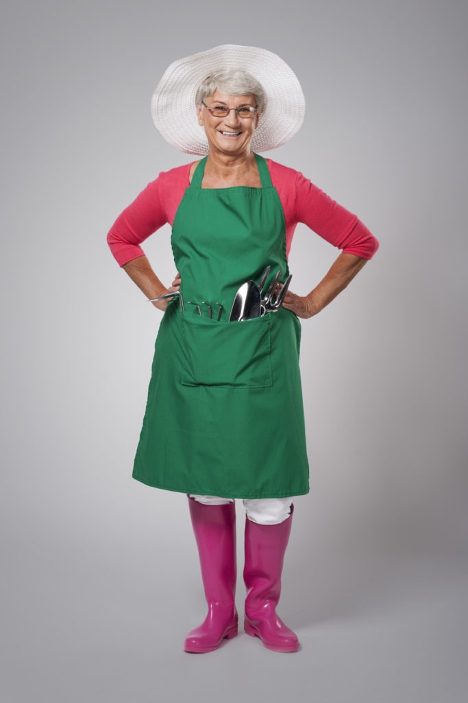  smiling elderly woman in green gardening apron with handy tools