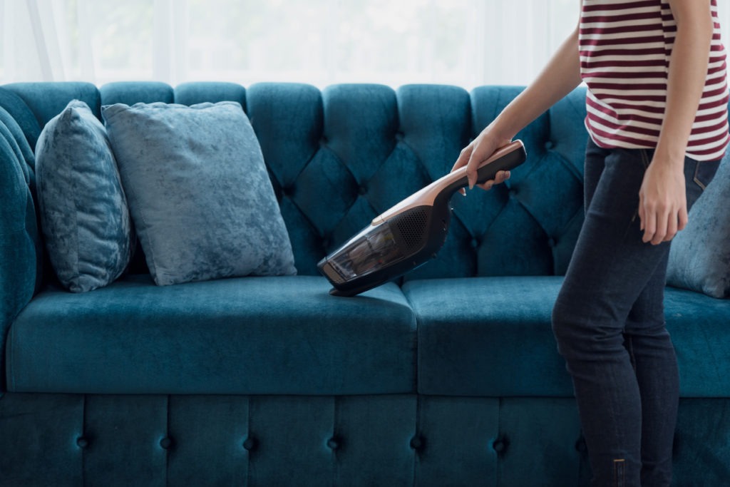 Woman housewife vacuuming furniture in a house with a hand-held portable vacuum cleaner