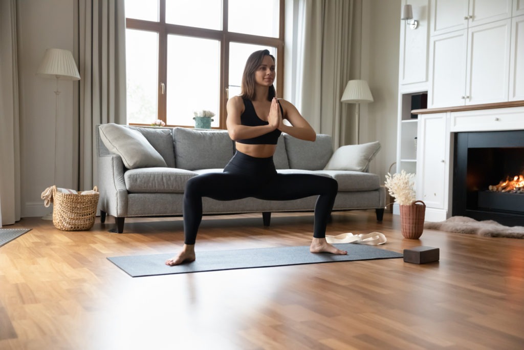 Woman standing on mat performing Goddess Pose in living room