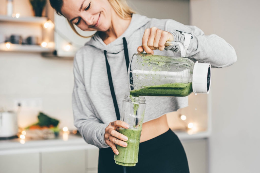 A woman pouring a green smoothie from the blender jar to the glass