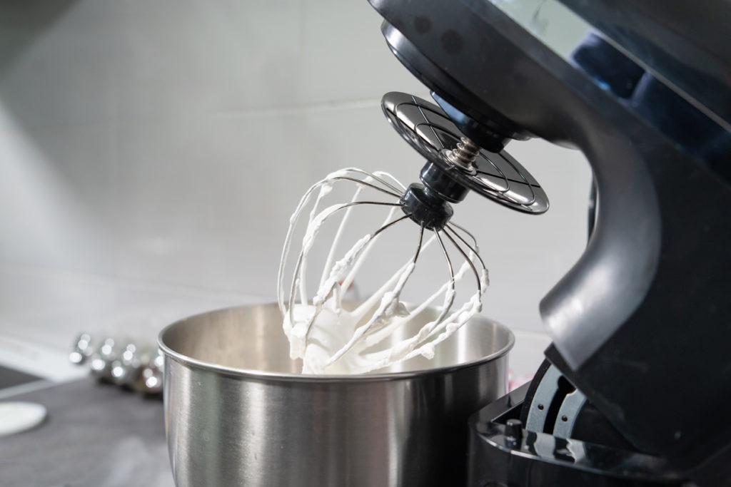 An open electric stand mixer with whipped white cream