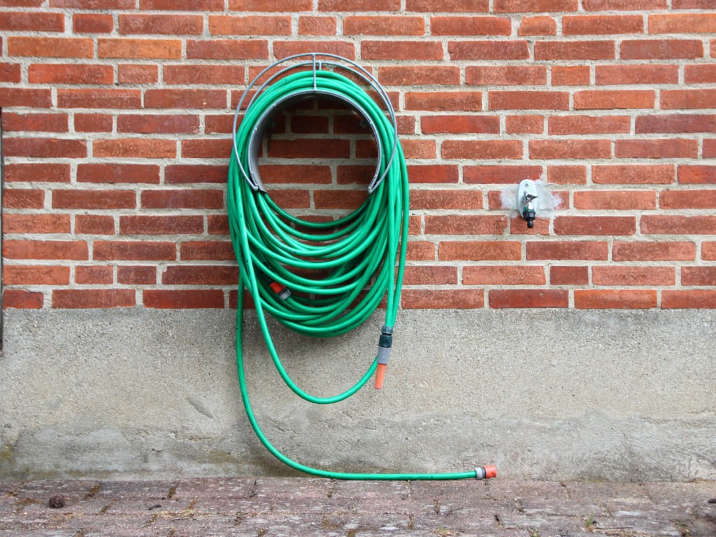 a long garden hose mounted on red brick wall