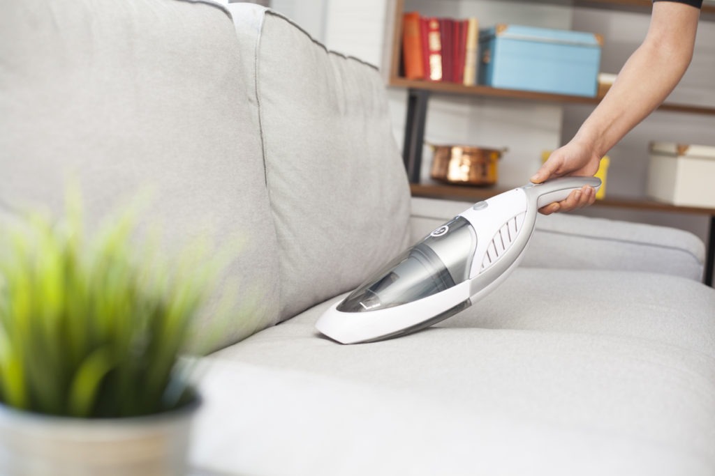 woman using handheld vacuum on sofa