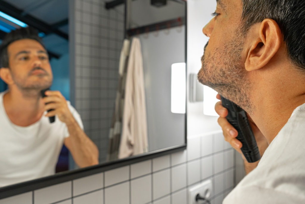 Man trimming his beard in front of a mirror.