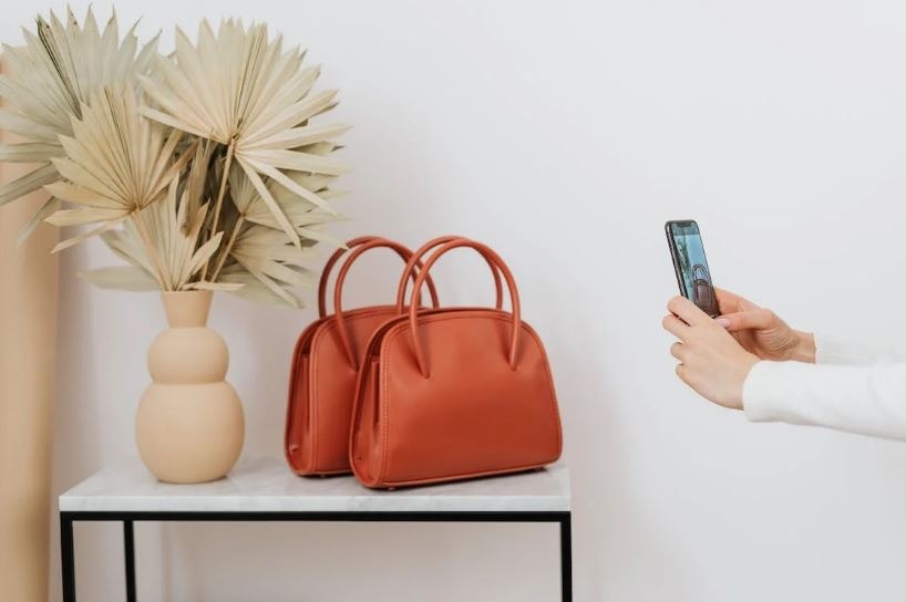 a person taking a photo of two orange leather handbags on a table next to a plant
