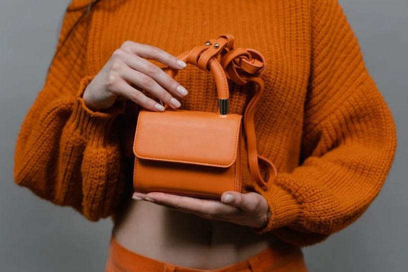 a small orange handbag held by a person wearing an orange crop-top sweater