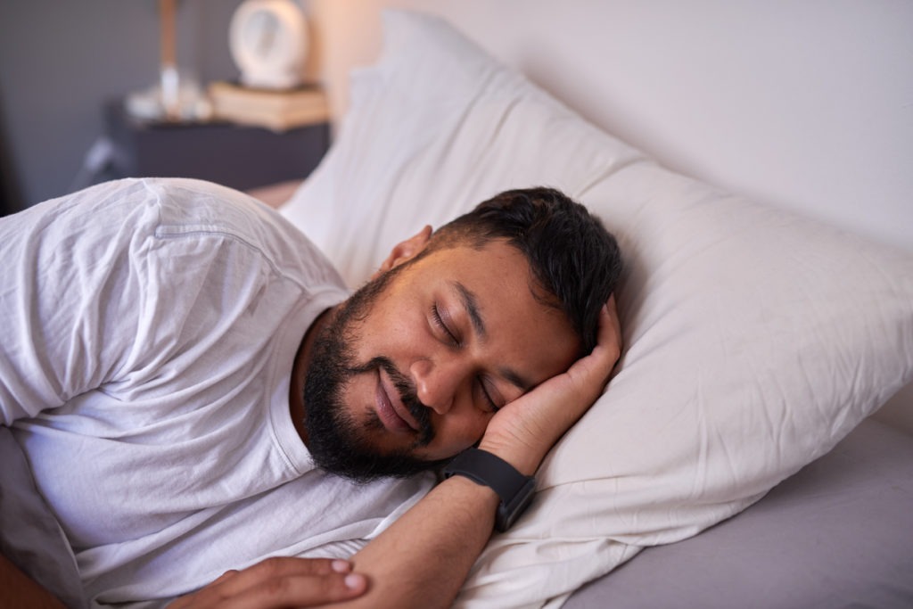 An adult man sleeps peacefully with a smile in bed in the morning
