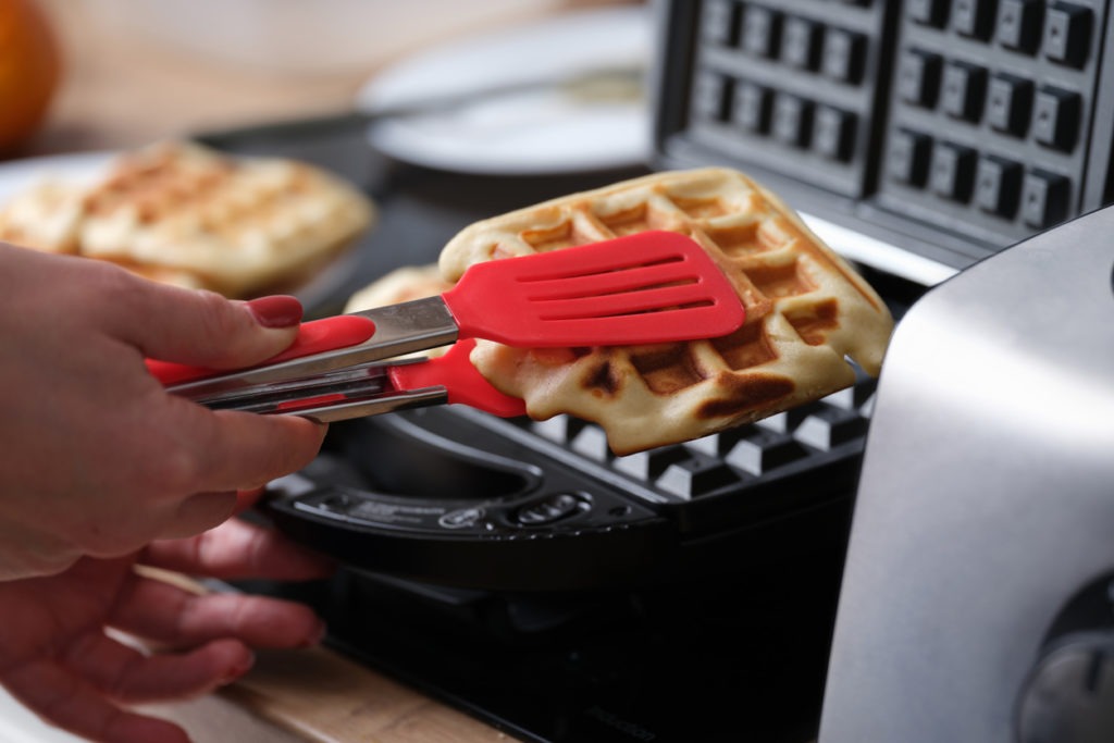 Cook taking out viennese waffle from multibaker using tongs closeup