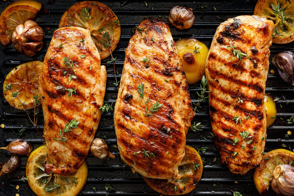 Grilled chicken breasts with thyme, garlic and lemon slices on a grill pan close up